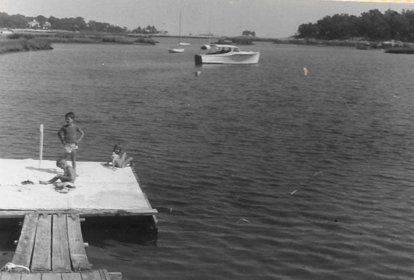 Children on the community dock at Salem Straits, with the tidal estuary, a moored boat, and the causeway beyond